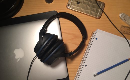 Photograph of notebook, headphones, tablet and cell phone on a desk