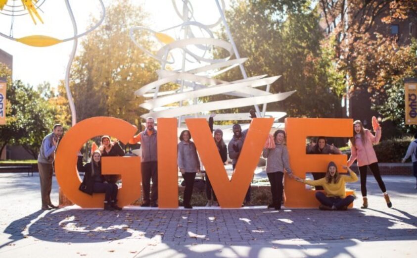 Students and Staff Celebrate Giving in a photograph surrounding a large GIVE sign on campus