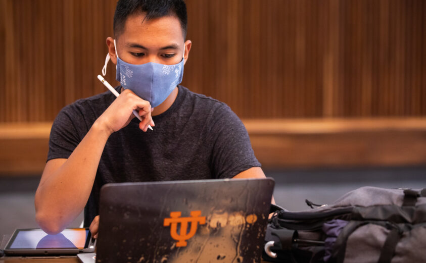 A masked student studies inside the Mossman Building at the start of the Fall Semester