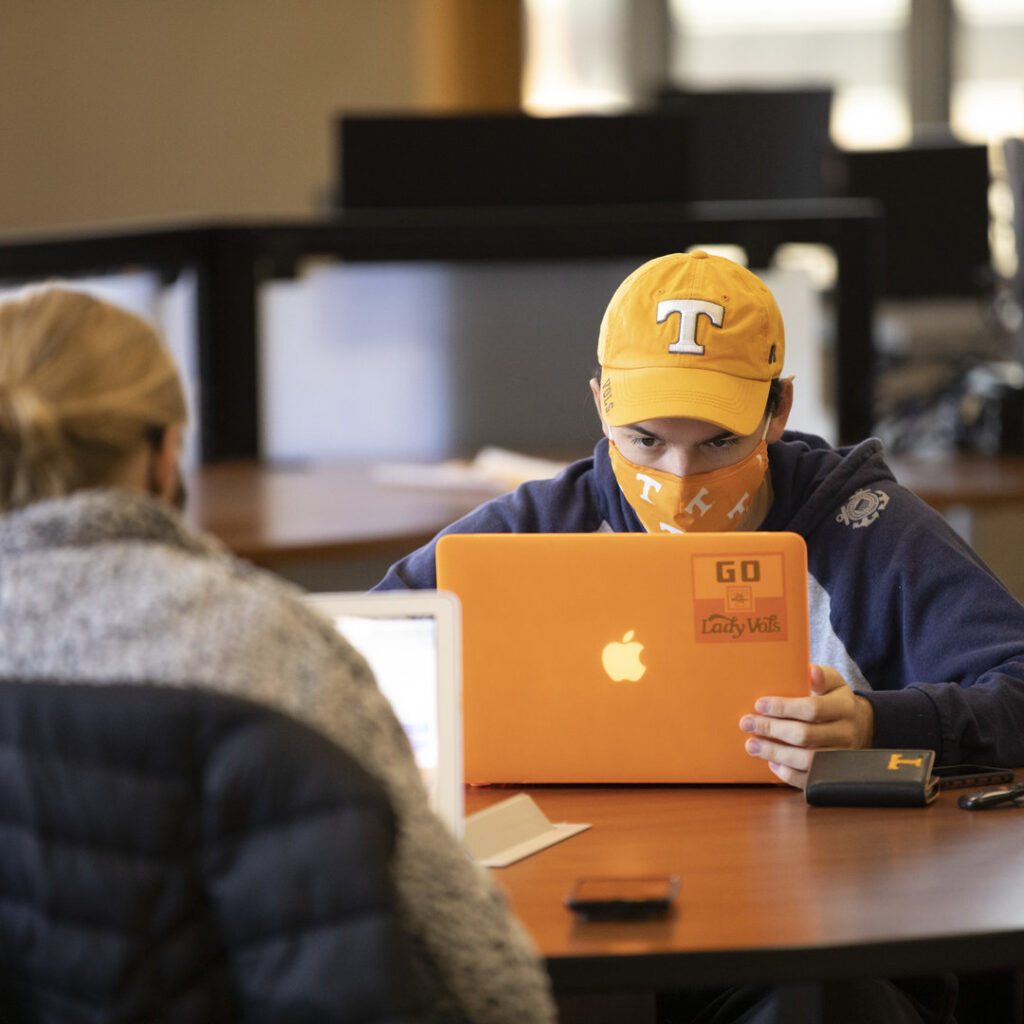 Student with a UT hat is using a laptop while seated at a desk in Hodges Library