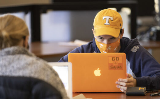 Student in a UT hat with laptop and mask studying in library