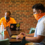 Two masked students are on their laptops studying