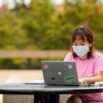 Student in a mask works on a computer outside