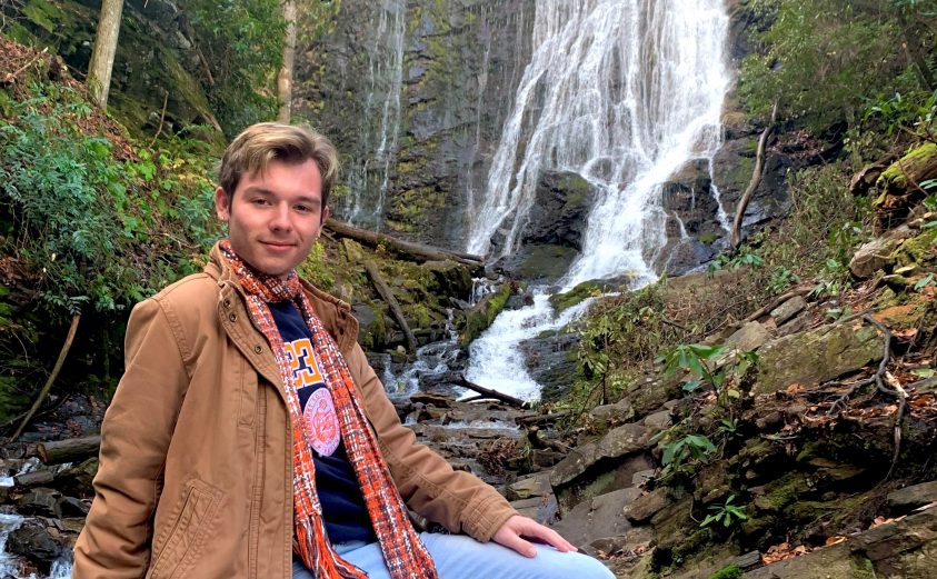 Student worker Evan Bushart posing in front of a waterfall