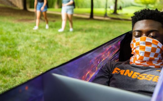 Image of a masked student using a laptop in a hammock