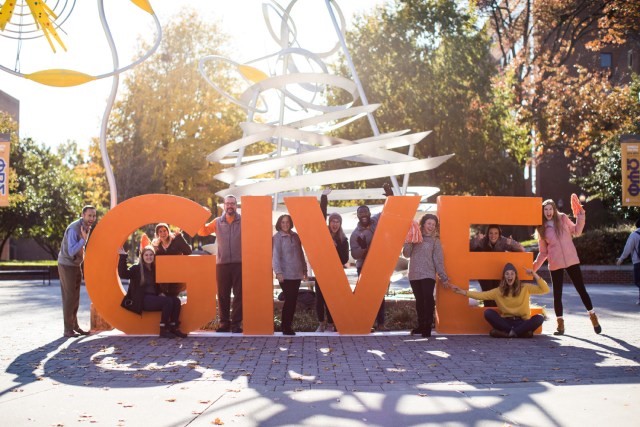 Picture of students and staff posing with a larger than life display of the word "Give"